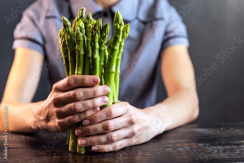 Asparagus in the hands against the background of a wooden black table with space for text