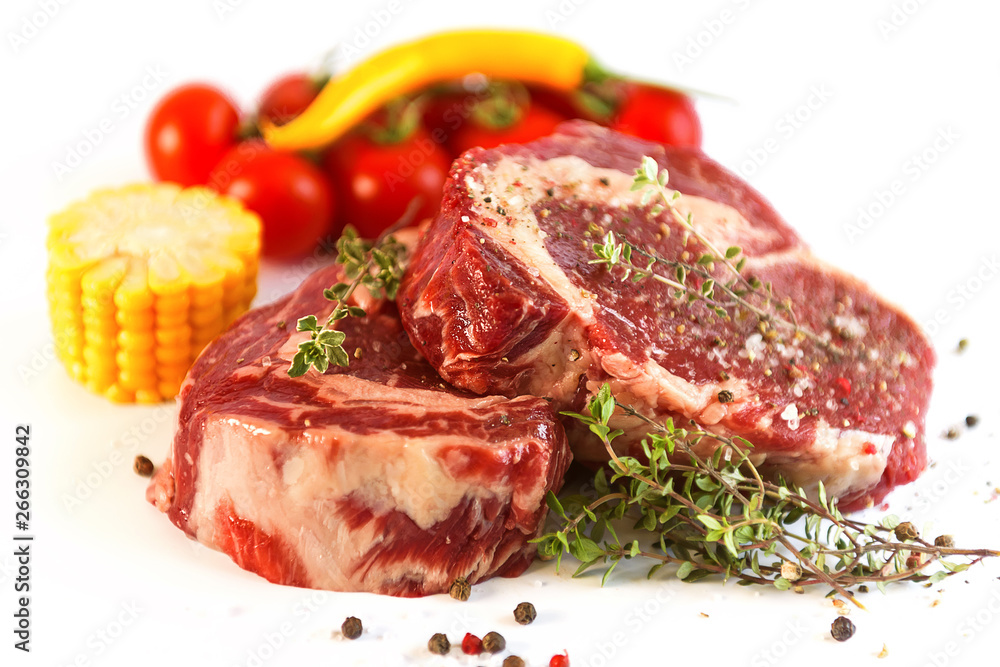 set for cooking a festive dinner for two. two raw marbled beef steaks, spices, vegetables and a grill pan with a meat fork. all on a white background