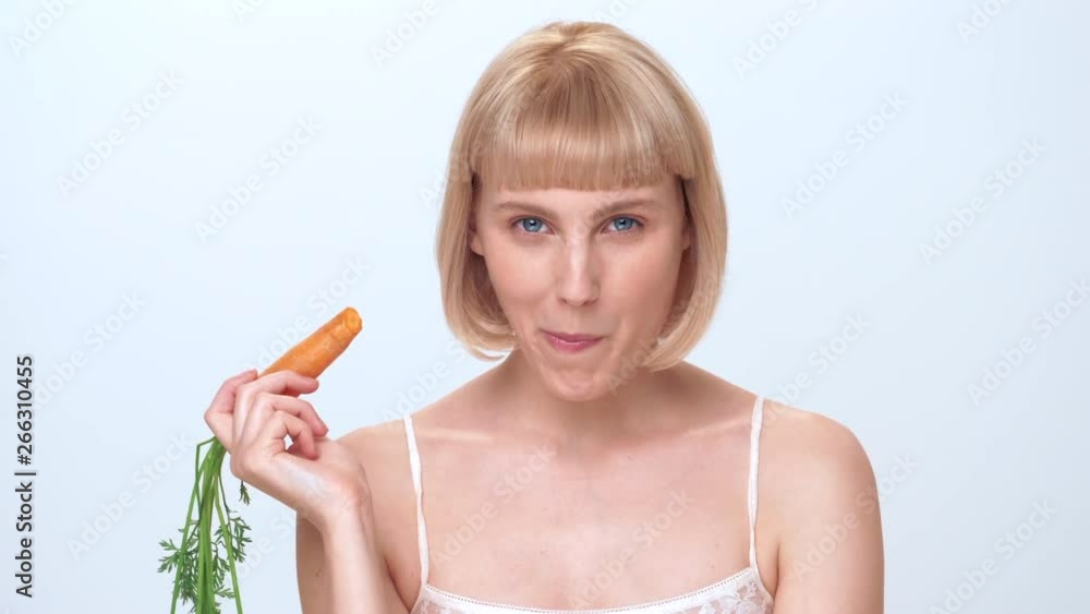 A beautiful young woman with blue eyes, blonde hair and a cute smile eats carrot to promote healthy living. A beautiful young woman with blue eyes, blonde hair and a cute smile eats carrot to promote healthy living.