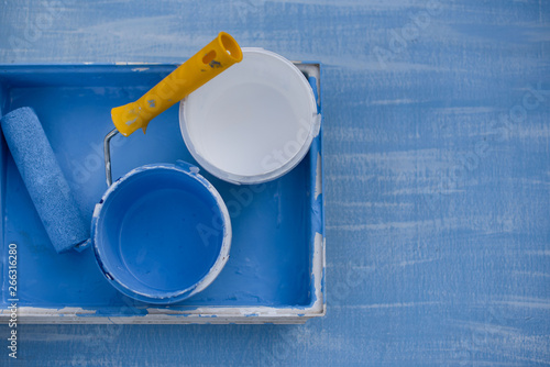 blue and white paint in cans top view. roller with a yellow handle for painting walls