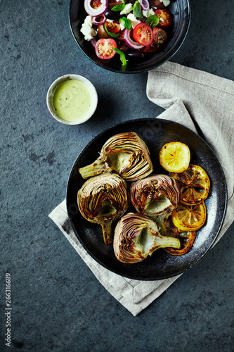 Roasted artichokes and lemons on a plate served with salad. Flat lay. Mediterranean cuisine