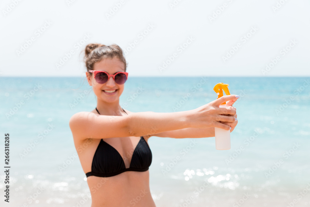 Young woman is holding a bottle of sunblock for body at the sea background Young woman is holding a bottle of sunblock for body at the sea background