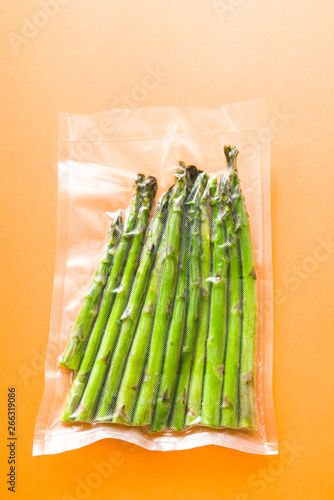 Vacuum sealed vegetables , asparagus, on a orange background top view, ready to be cooked with sous vide rooner photo