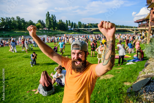 Fan zone. Entertainment concept. Visit summer festival. Summer fest. Hipster in cap happy celebrate event fest or festival. Man bearded hipster in front of crowd. Open air concert. Music festival