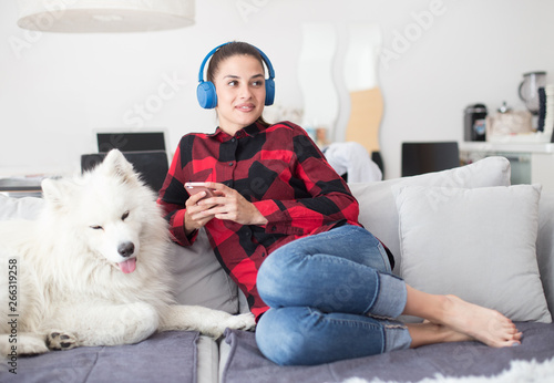 Young woman with headphones sitting on sofa with dog