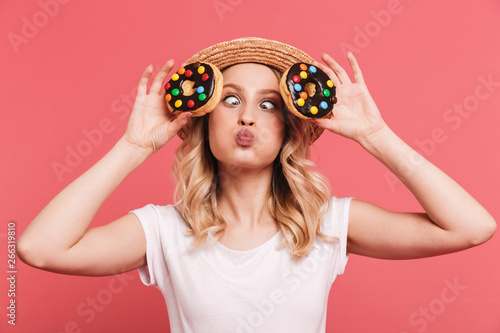 Portrait of content blond woman 20s wearing straw hat laughing while holding tasty sweet donuts