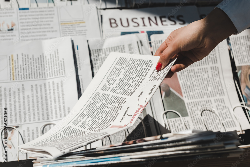 partial view of woman taking daily print newspaper from stand partial view of woman taking daily print newspaper from stand