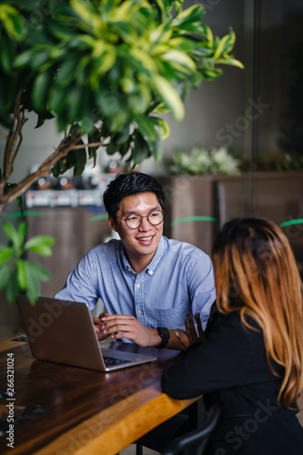 A handsome looking Asian man talking to a team mate inside a cafe. He is looking good in his blue polo.
