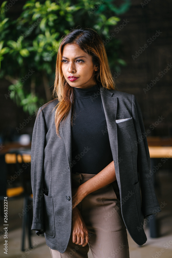 Mid shot Portrait of a beautiful,tanned millennial Malay Asian woman sophisticatedly looking in a business outfit standing inside the city restaurant during the day.