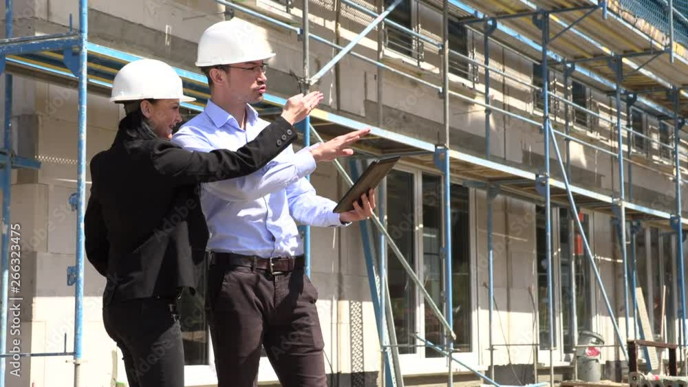 Two architects in white helmets discuss a plan at a construction site Two architects in white helmets discuss a plan at a construction site