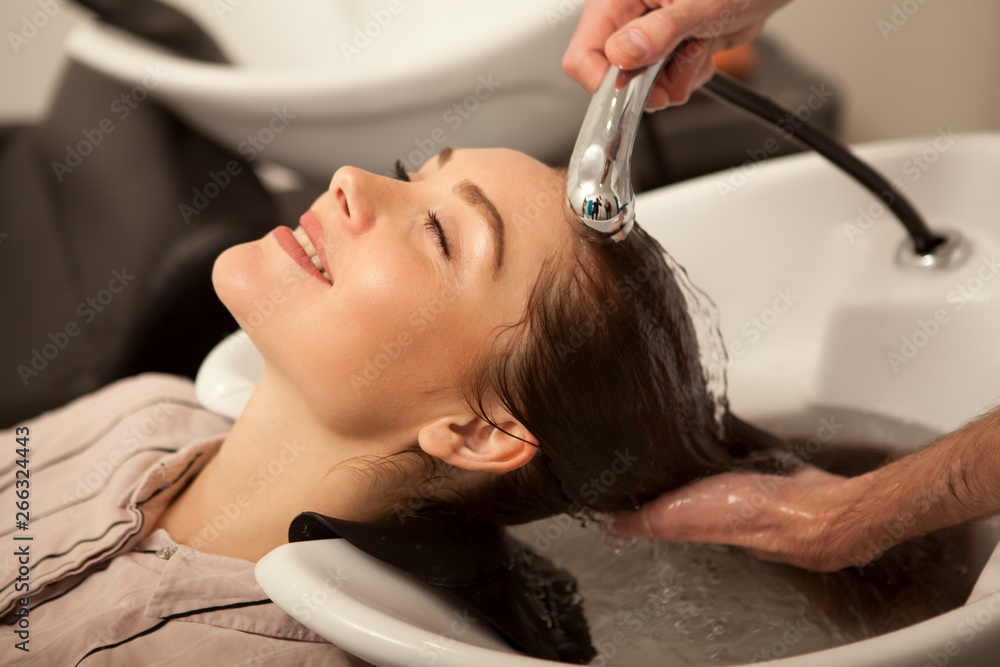 Fototapeta premium Happy beautiful woman smiling with her eyes closed while professional hairdresser washing her long healthy hair. Attractive woman enjoying relaxing hair treatment at beauty salon