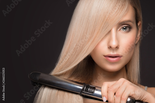 Beautiful blond girl with a perfectly smooth hair, classic make-up with curling styler in the hands. photo