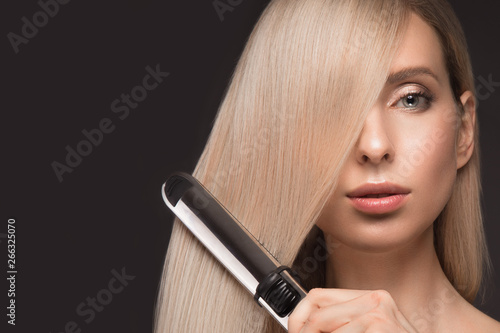 Beautiful blond girl with a perfectly smooth hair, classic make-up with curling styler in the hands. photo