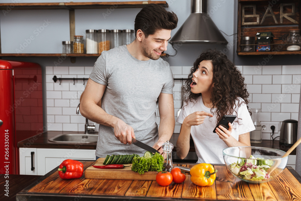 Picture of happy couple cooking salat with vegetables together in modern kitchen at home Picture of happy couple cooking salat with vegetables together in modern kitchen at home
