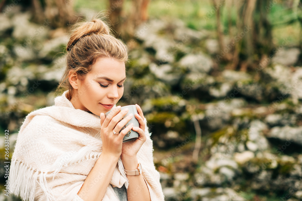 Beautiful woman holding cup of coffee or tea, covered with beige big scarf, posing outdoors Beautiful woman holding cup of coffee or tea, covered with beige big scarf, posing outdoors