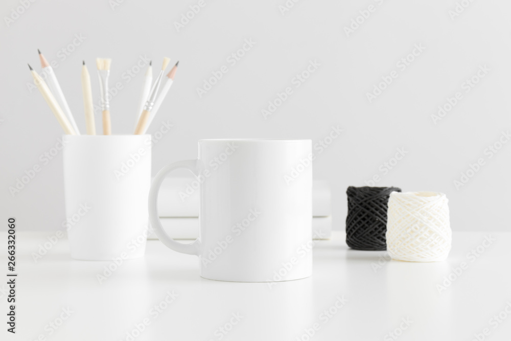 Naklejka premium Mug mockup with workspace accessories on a white table.
