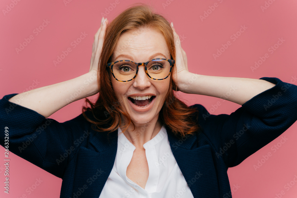 Photo of positive redhead female office worker keeps palms on ears, looks happily at camera, wears formal outfit, isolated over pink background. People, positive emotions and facial expressions Photo of positive redhead female office worker keeps palms on ears, looks happily at camera, wears formal outfit, isolated over pink background. People, positive emotions and facial expressions