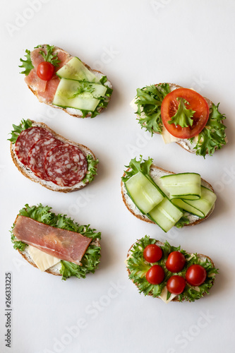 Fresh sandwiches with sausage, cheese, bacon, tomatoes, lettuce, cucumbers on a light background. Vertical orientation