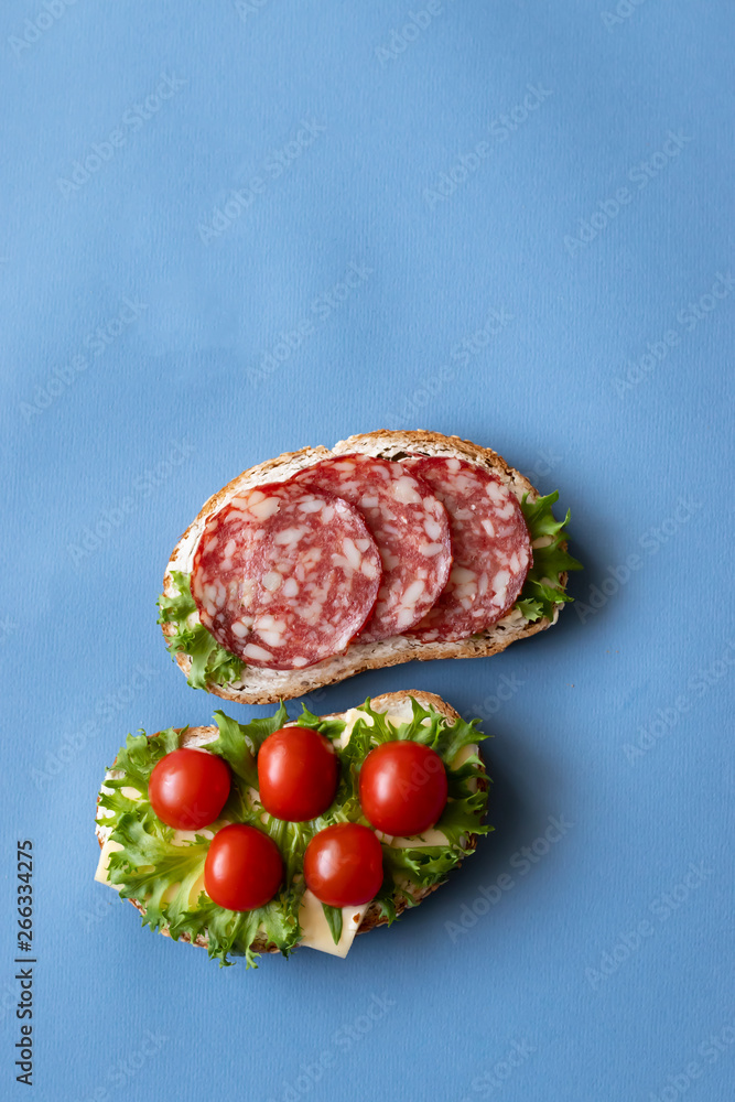 Fresh sandwiches with sausage, cheese, bacon, tomatoes, lettuce, cucumbers on a blue background. Vertical orientation Fresh sandwiches with sausage, cheese, bacon, tomatoes, lettuce, cucumbers on a blue background. Vertical orientation
