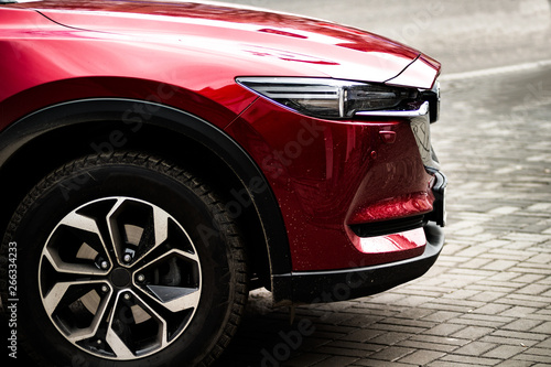 The front side of a red car with a large bright wheel standing on a wet asphalt. Background.