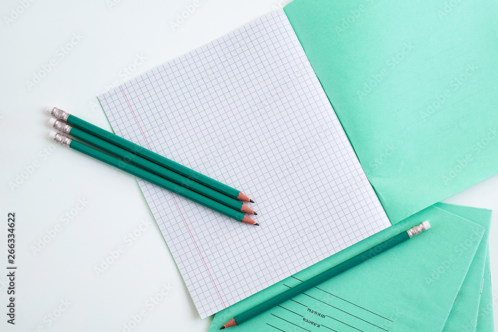 On the table is an open notebook in a cage. Pencils next to the school notebook. Notebook for schoo On the table is an open notebook in a cage. Pencils next to the school notebook. Notebook for schoo