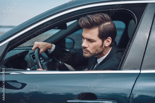 Stuck in traffic. Handsome young man in full suit looking straight while driving a car © gstockstudio