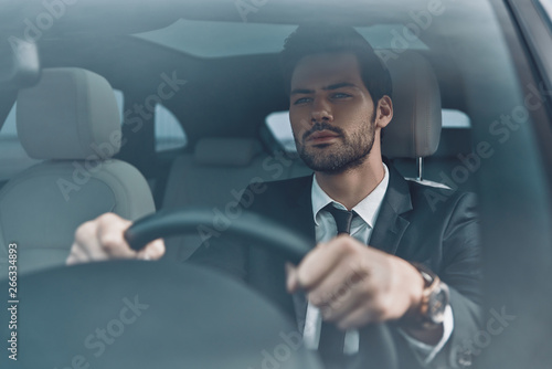 Looking forward. Handsome young man in full suit looking straight while driving a car © gstockstudio