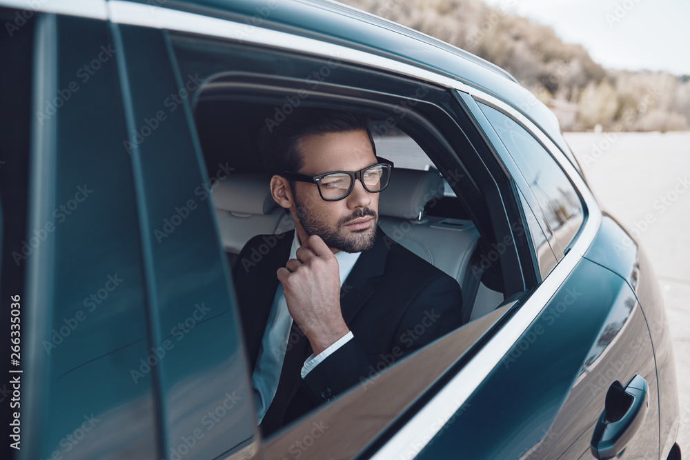 Thinking about... Thoughtful young businessman keeping hand on chin while sitting in the car Thinking about... Thoughtful young businessman keeping hand on chin while sitting in the car