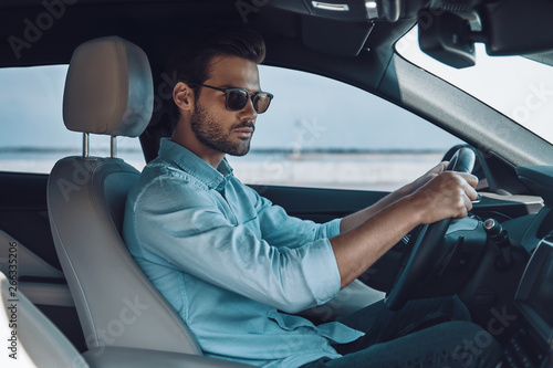 Driving his new car. Handsome young man in smart casual wear looking away while driving a status car © gstockstudio