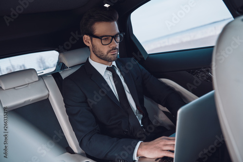 Young and successful. Handsome young man in full suit working using laptop while sitting in the car © gstockstudio