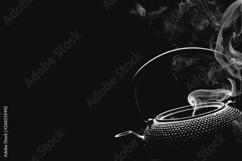 Rustic teapot on black background. Steaming tea kettle. Cooking concept.