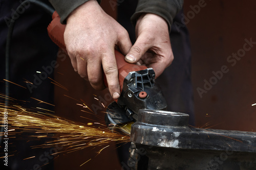 Close up of male worker hand cutting metal pipe with electric grinder, orange sparks flying during working with steel at workshop. Dangerous work concept.