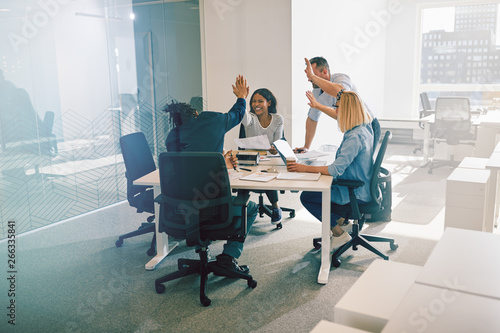 Fotografie Diverse work colleagues excitedly high fiving during an office m