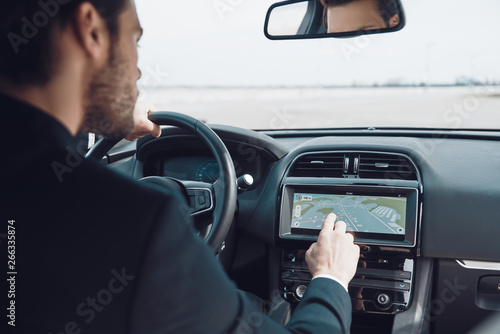 Getting around the city. Rear view of young man in full suit using global positioning system device to check the map while driving a car