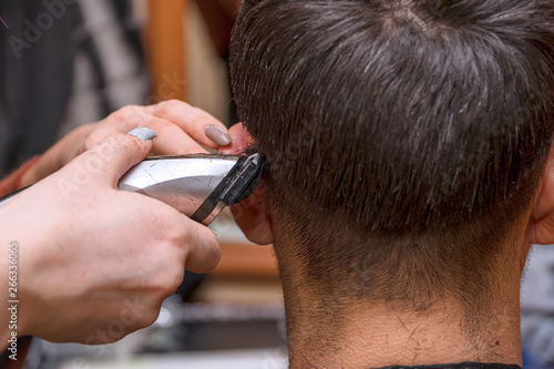 Woman Hairdresser cuts man's hair with electric clipper trimmer