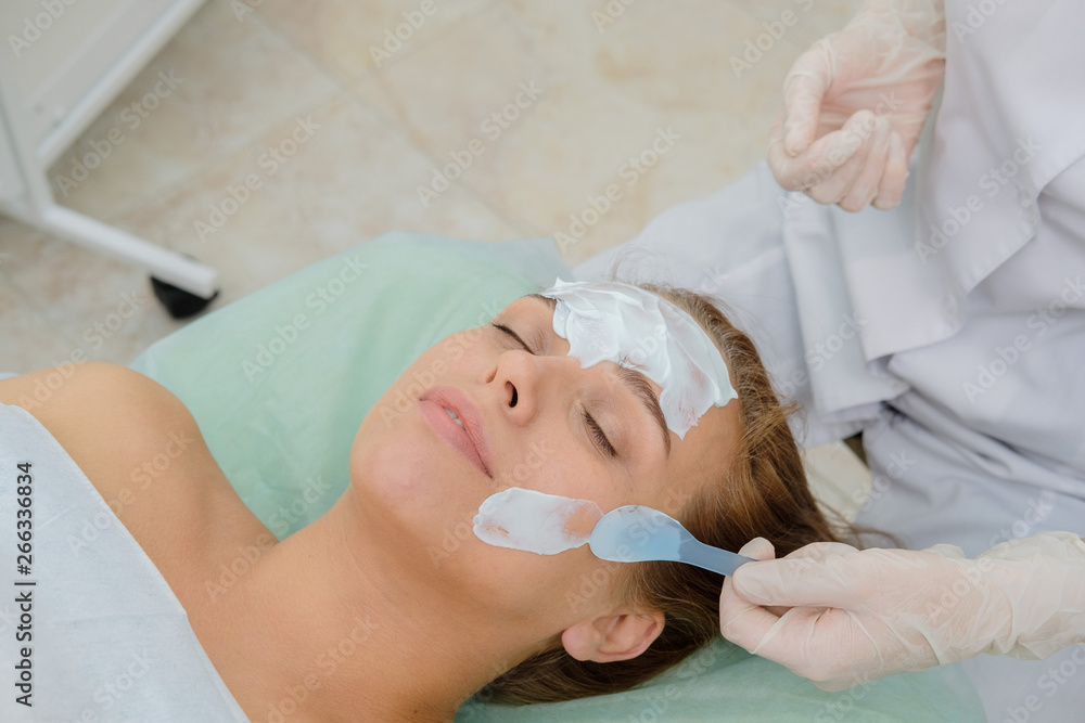 Face peeling mask, spa beauty treatment, skincare. Woman getting facial care by beautician at spa salon. Сosmetologist applying  cream mask on face of a girl patient. Cosmetology.  Close up