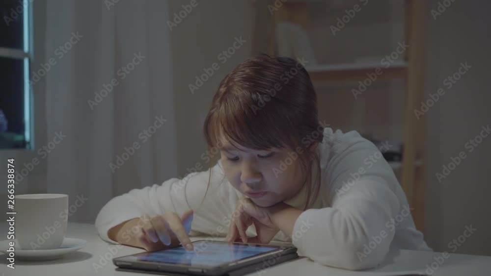 Young asian woman working late using tablet checking social media while relax on desk in night in living room at home. Enjoying time at home concept. Young asian woman working late using tablet checking social media while relax on desk in night in living room at home. Enjoying time at home concept.
