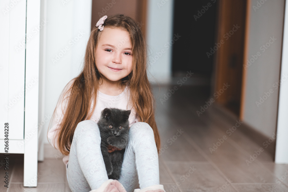 Smiling kid girl 4-5 year old holding small kitten sitting on floor in room. Looking at camera. Childhood. Smiling kid girl 4-5 year old holding small kitten sitting on floor in room. Looking at camera. Childhood.