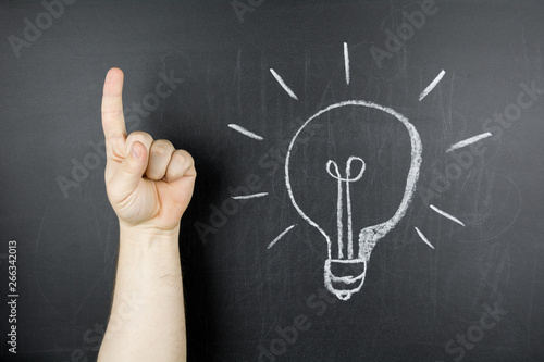 Getting new idea. Teacher, educator, trainer or student pointing up with finger. Light bulb on chalkboard.