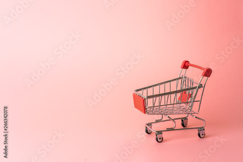 Red miniature trolley from a supermarket on a pink background. Close-up.