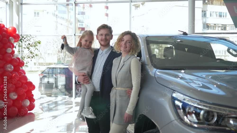 portrait of happy consumer family couple with kid girl on hands shows keys to new car purchased at auto showroom portrait of happy consumer family couple with kid girl on hands shows keys to new car purchased at auto showroom