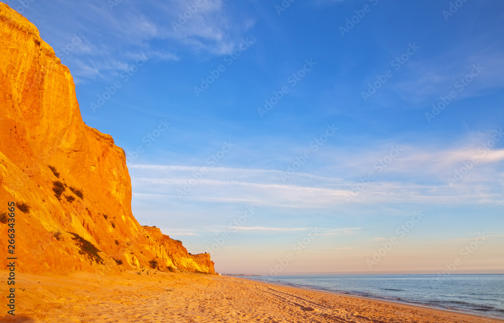 Portugal. Algarve. Vilamoura. The famous Falesia Beach with a shallow sandy beach of the Atlantic Ocean, bordered by unusual red rocks at sunset. Summer vacation by the sea. Natural background