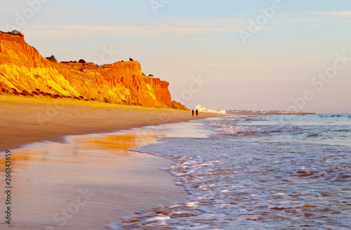 Beautiful Praia da Falesia near the city of Vilamoura with a shallow sandy beach fringed with unusual red rocks at sunset. Algarve, Portugal. Natural background. Summer holiday by the sea photo