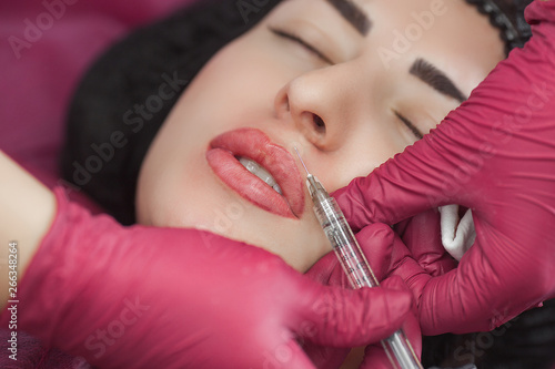 Cosmetologist making procedure. Dermatologist making an injection of botox or hyaluronic acid. Close up still of lip injection. Lip booster procedure. Beauty salon service.