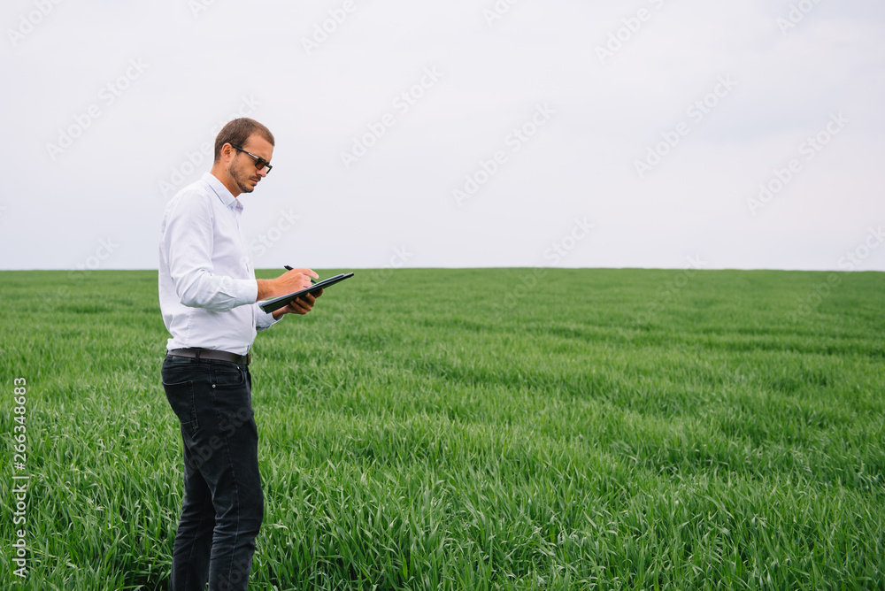 Young agronomist holds laptop in green wheat field. Agribusiness concept. agricultural engineer standing in a wheat field with a tablet in summer Young agronomist holds laptop in green wheat field. Agribusiness concept. agricultural engineer standing in a wheat field with a tablet in summer