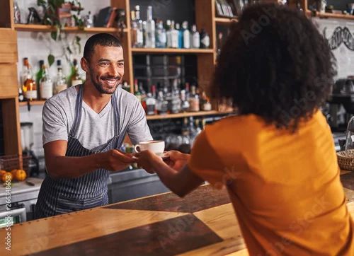 Naklejka na ścianę Męski barista podaje filiżankę kawy kobiecemu klientowi w kawiarni