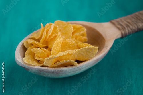 Cornflakes in a wooden spoon on a green background