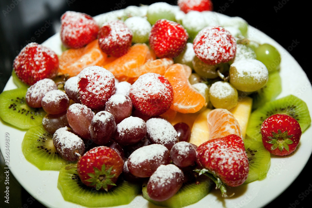 Obraz premium Ripe berries and fruit powdered with powdered sugar on a plate close-up