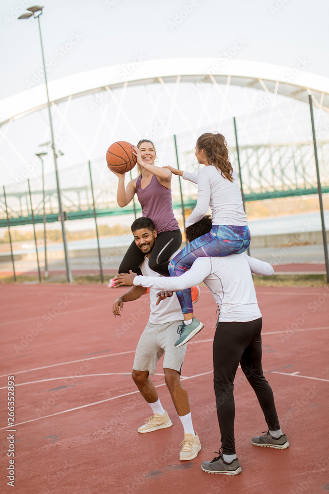 Young women sitting on the men shoulders and holding a basketball at outdoor court