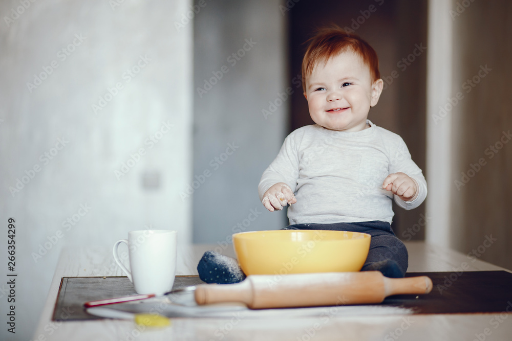 little boy sitting at home on a table in the kitchen near a plate of flour little boy sitting at home on a table in the kitchen near a plate of flour